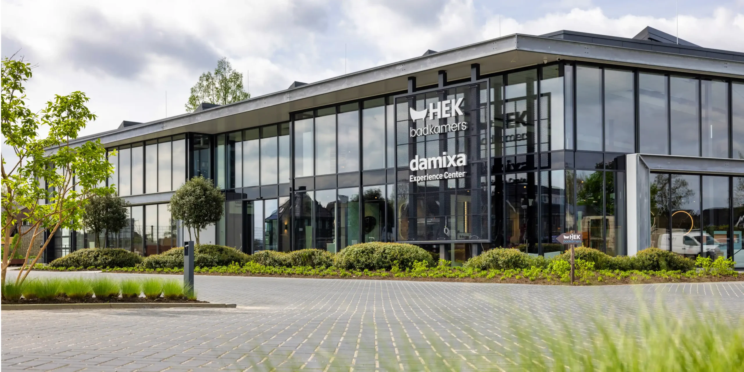 De moderne glazen gevel van het HEK badkamers en Damixa Experience Center met veel ramen, groen en een uitnodigende entree waar geurbeleving de bezoeker verwelkomt.
